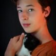 A teenager gently holding a black and white guinea pig against a dark background.